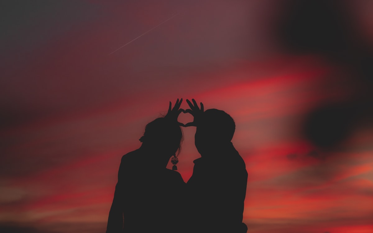 Silhouette of a couple forming a heart shape with their hands against a purple sky